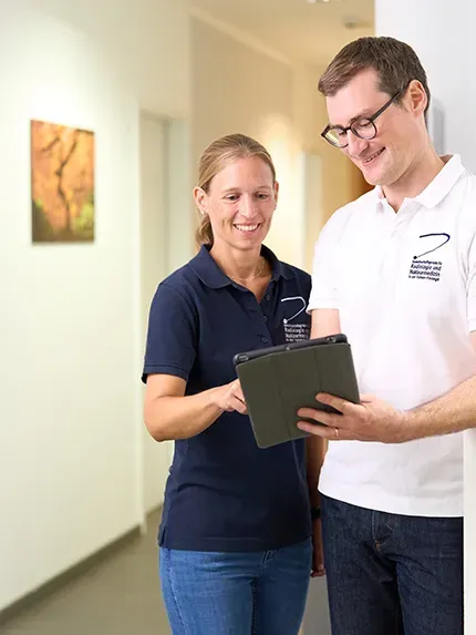 Zwei Mitarbeitende der Praxis für Radiologie und Nuklearmedizin in der Kaiser-Passage besprechen Untersuchungsergebnisse auf einem Tablet im Flur der Praxis.